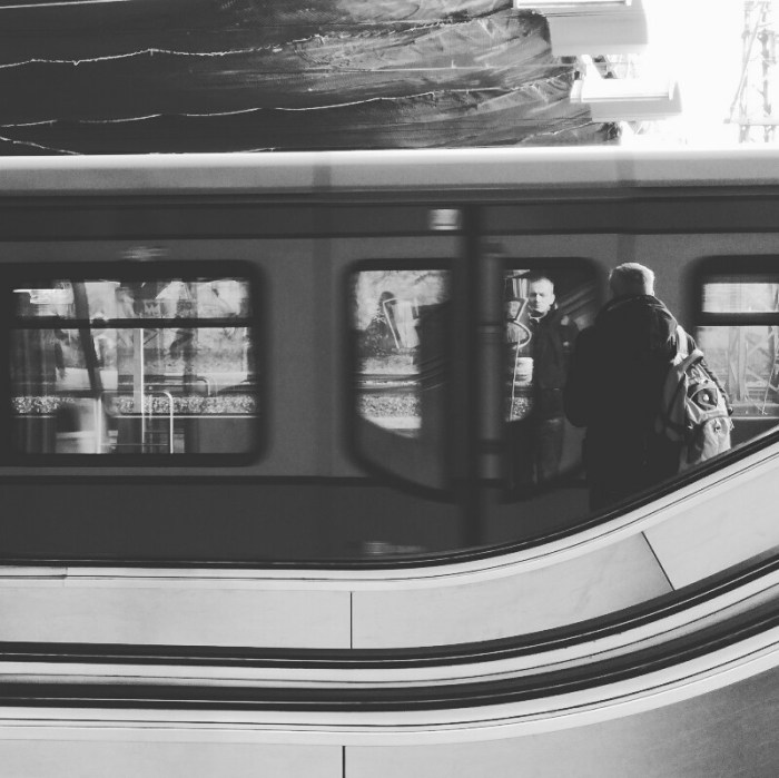 Street photo of a man's reflection on a moving train window