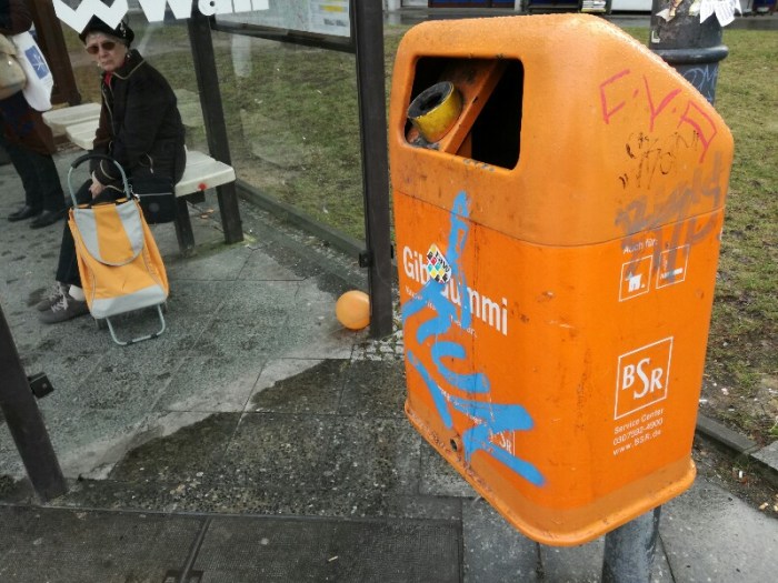 Three random orange objects at a bus stop - streetphoto by Stefan Klenke